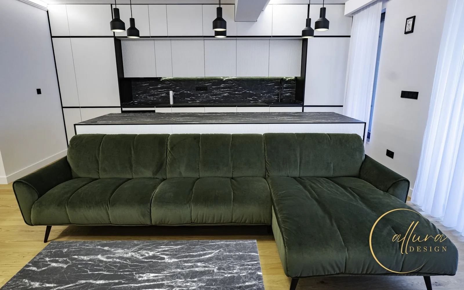 Living open-space cu colțar din catifea verde, în fața unei bucătării alb-negru cu insulă