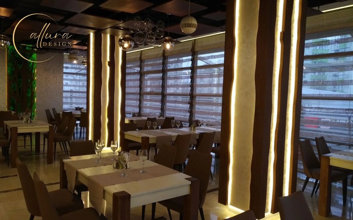 Sală de restaurant cu stâlpi placați cu lemn, conturați cu lumină caldă, și mese pregătite pentru servire